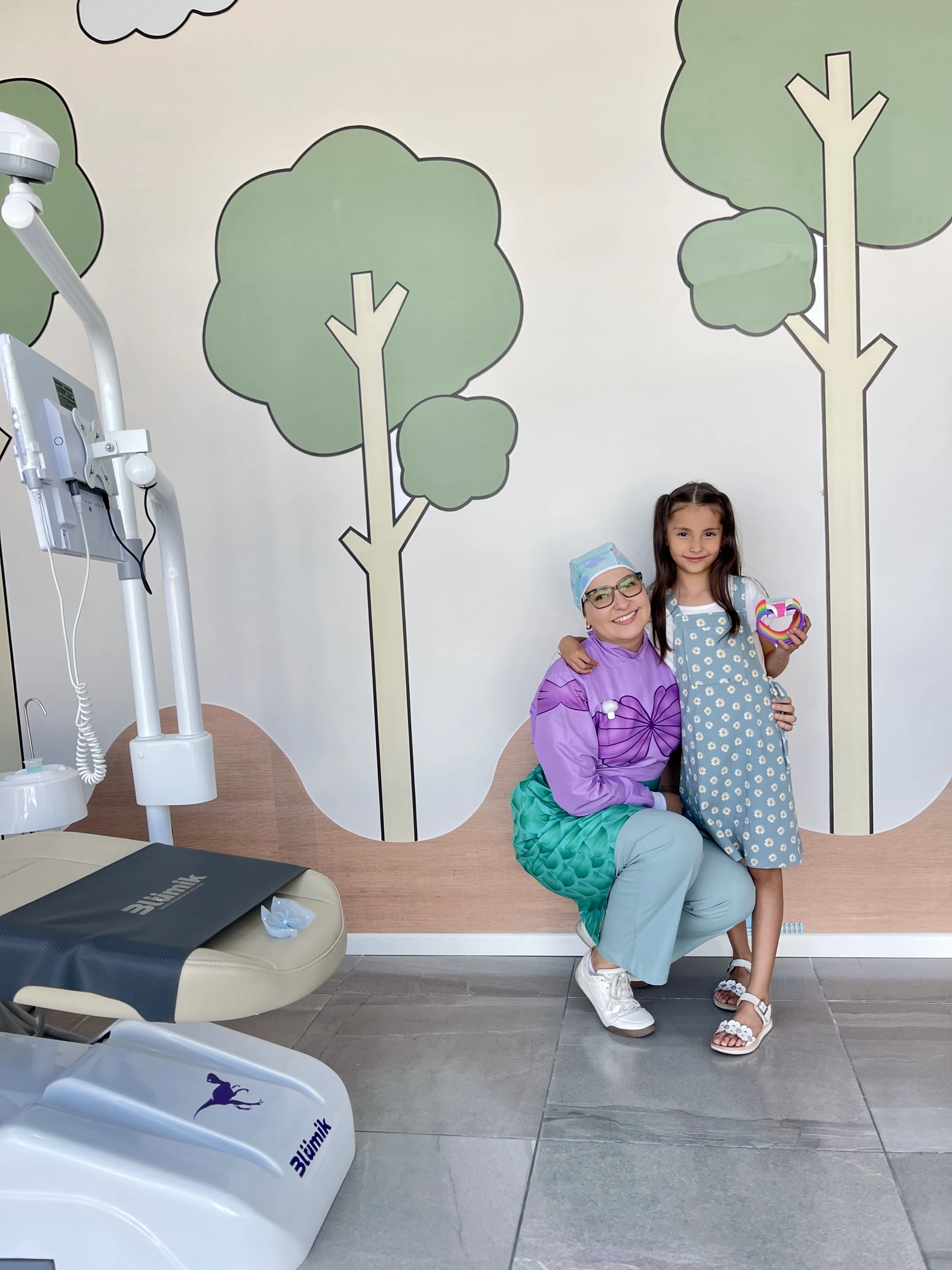 Odontopediatra con uniforme morado junto a una niña